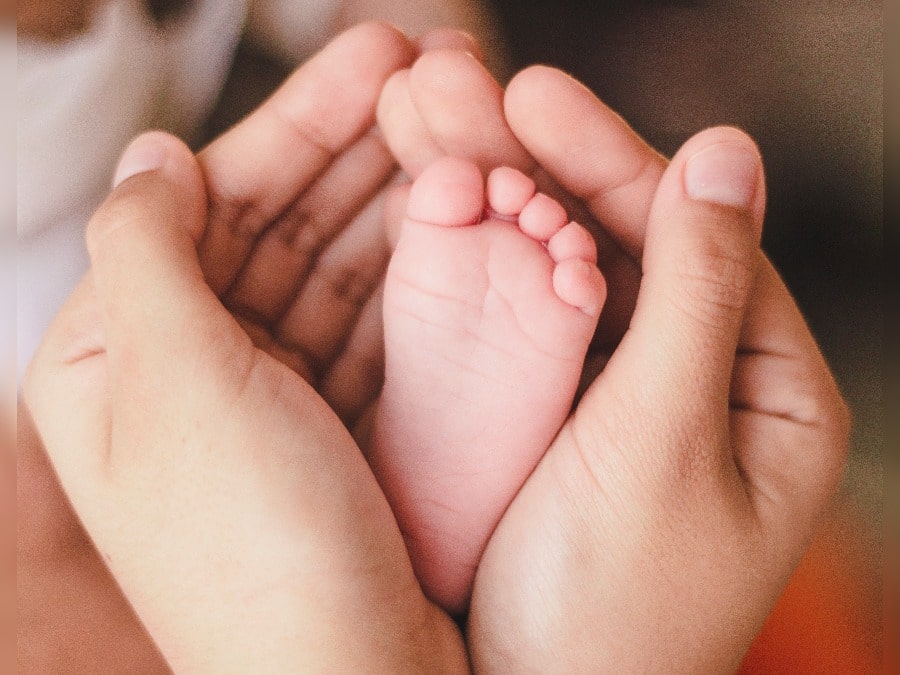 Die Hände einer Mutter umschließen die Füße eines Babys.