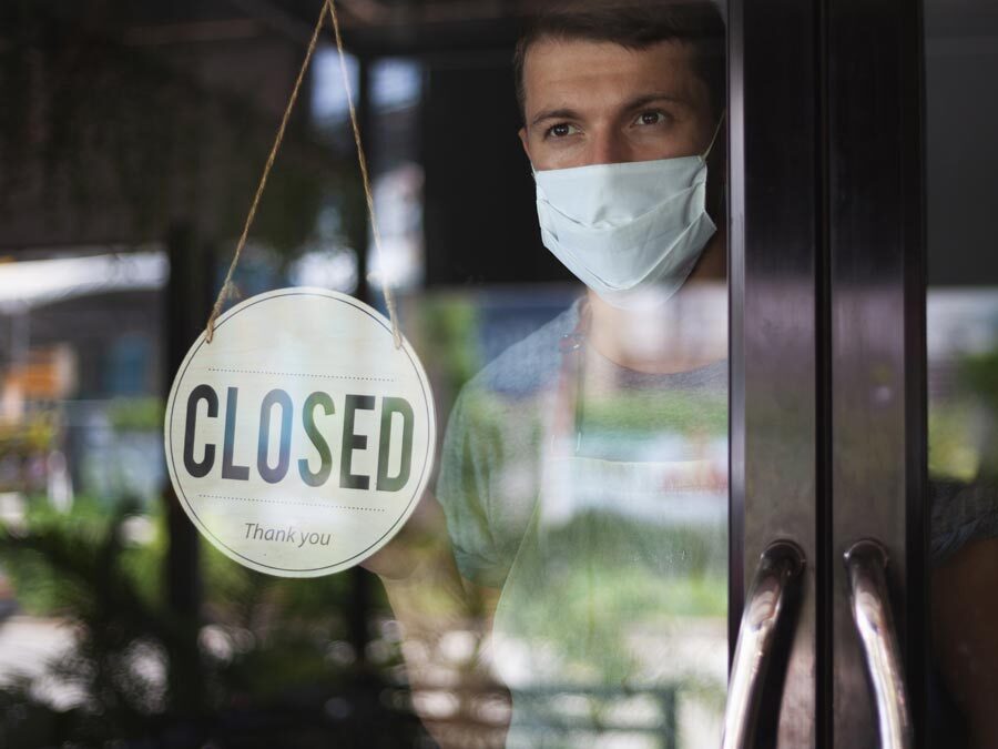 Ein geschlossener Laden mit dem Schild "closed". Drin befindet sich ein Mann mit Maske.