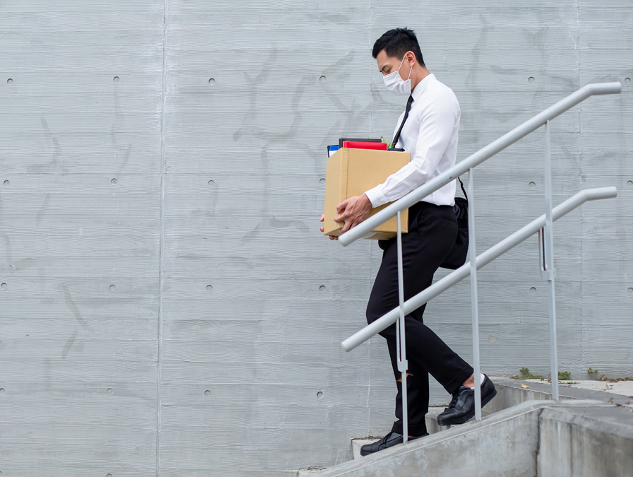 Ein Arbeitnehmer trägt einen Karton mit persönlichen Sachen aus dem Büro. Sein Blick ist niedergeschlagen.