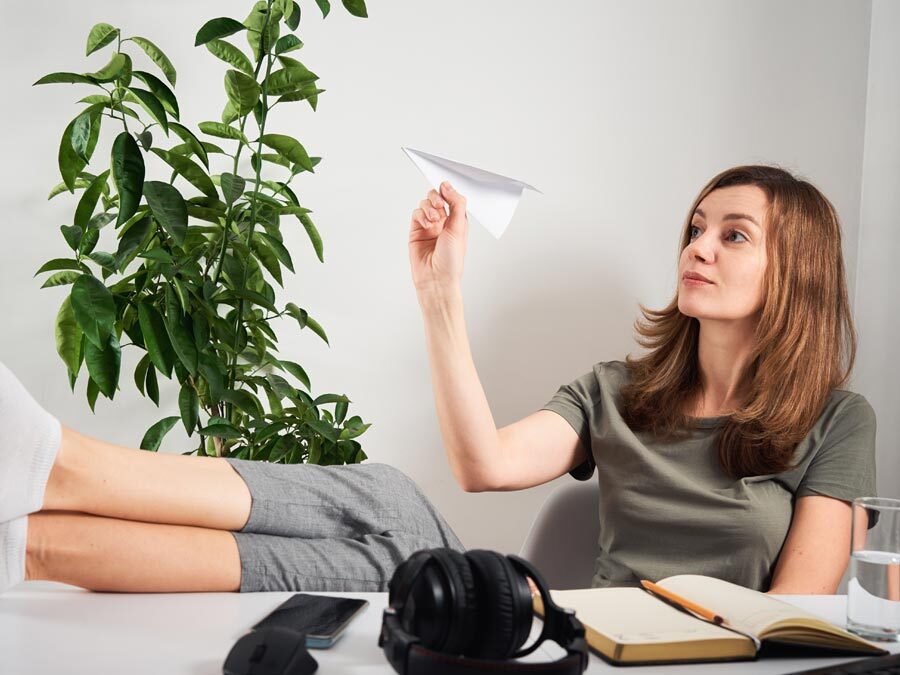 Eine Frau sitzt im Büro und lässt einen Papierflieger fliegen. Sie hat ein Bore-Out-Syndrom.