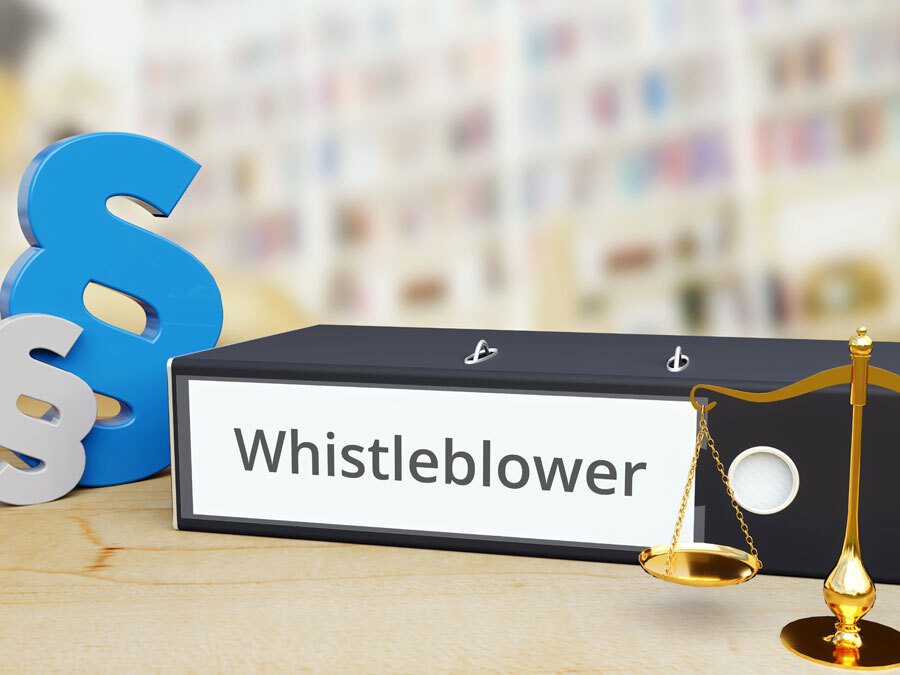Paragraphenzeichen eine Waage und ein Ordner mit der Aufschrift Whistleblower symboliseren die Pflichten nach dem Hinweisgeberschutzgesetz.