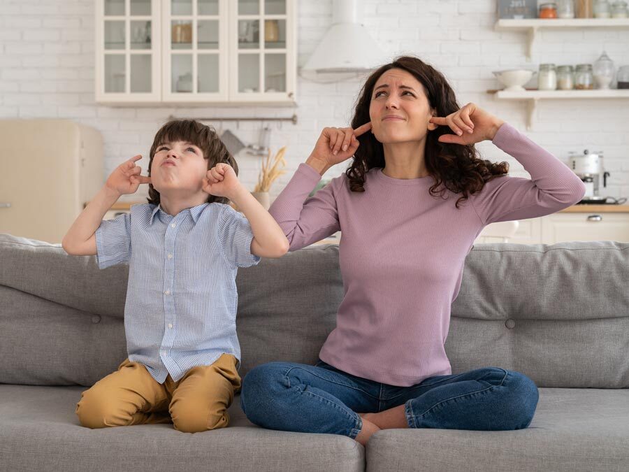Mutter und Sohn sitzen auf dem Sofa und halten sich die Ohren zu.