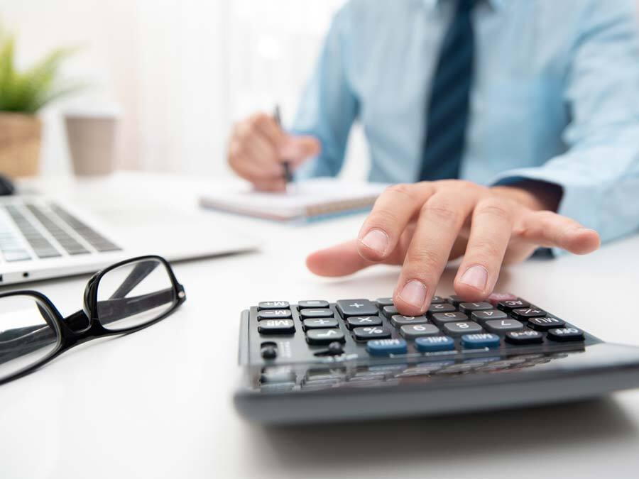 Ein Erbe tippt auf einen Taschenrechner. Er macht für den verstorbenen Erblasser eine Steuererklärung nach dem Tod.