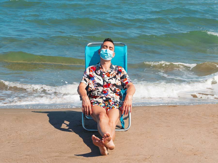 Arbeitnehmer verbringt Strandurlaub mit Maske, weil der Chef Betriebsurlaub wegen Corona anordnet.