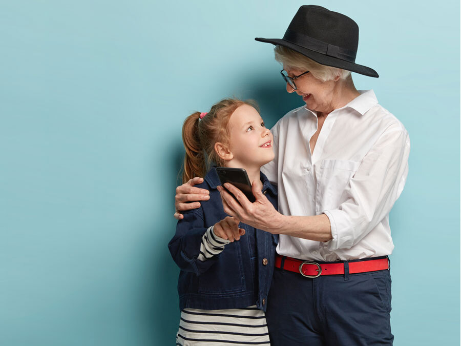 Eine ältere Dame hält ihre Enkelin im Arm. In der Hand hat sie ein Smartphone.