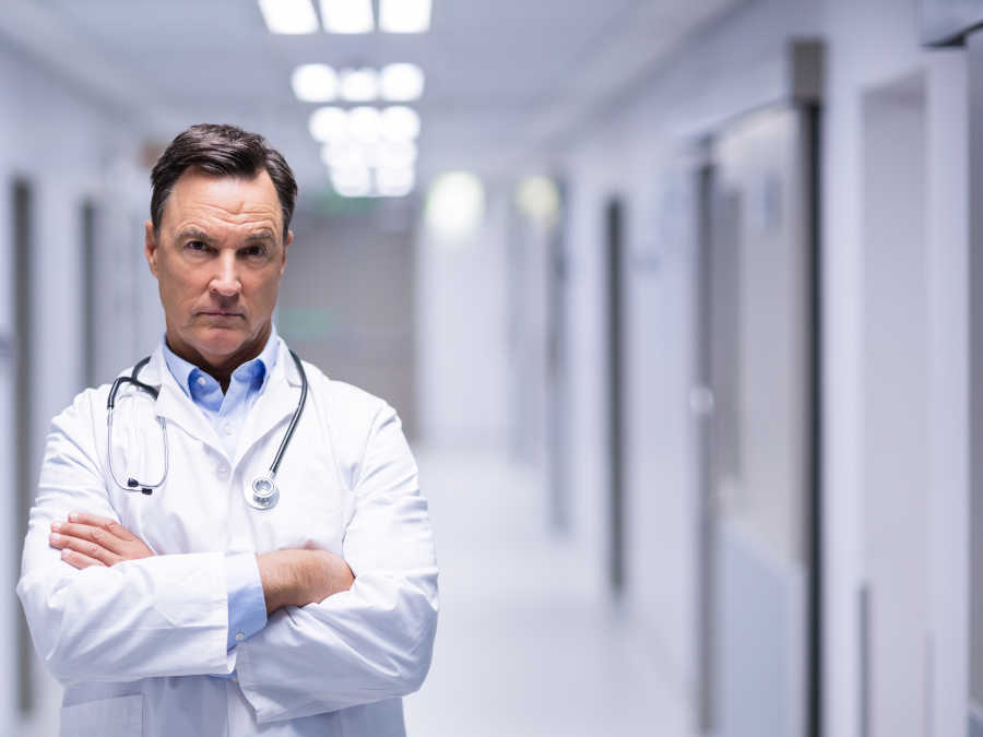 Ein Arzt mit besorgtem Blick steht im Flur eines Krankenhauses.