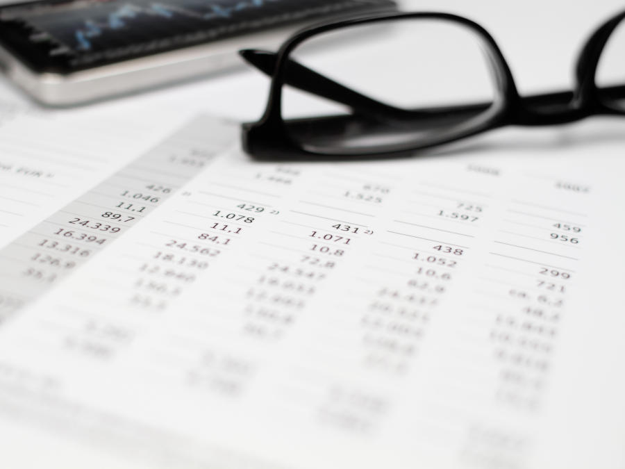 Eine lange Tabelle mit Zahlen und eine Brille liegen auf dem Tisch. Ein Arbeitnehmer der Kurzarbeitergeld bezogen hat muss Steuern nachzahlen.