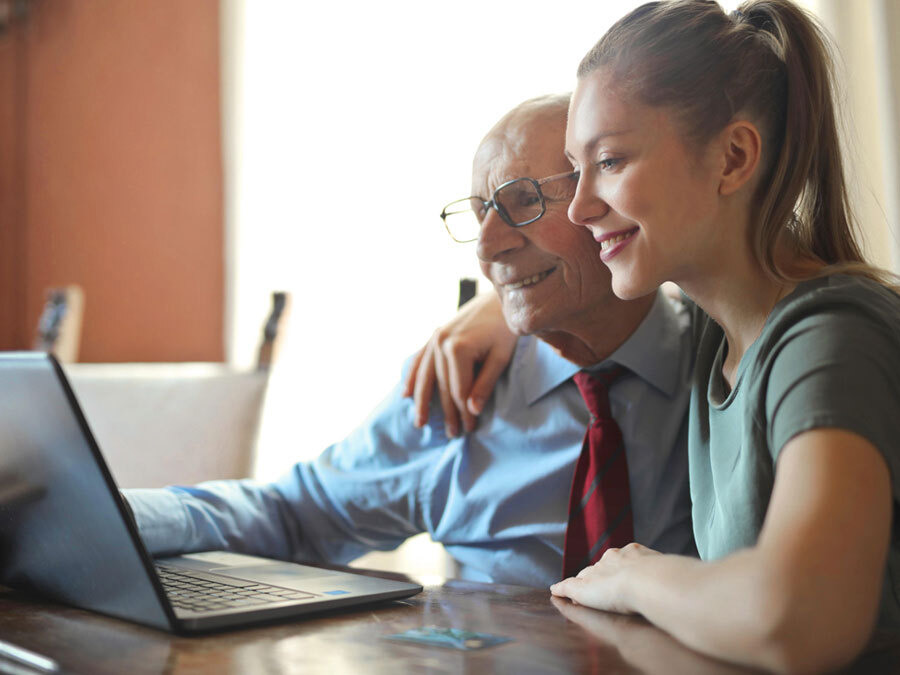 Ein älterer Herr sitzt mit seiner Tochter am Rechner. Sie prüfen den Pflegevertrag.