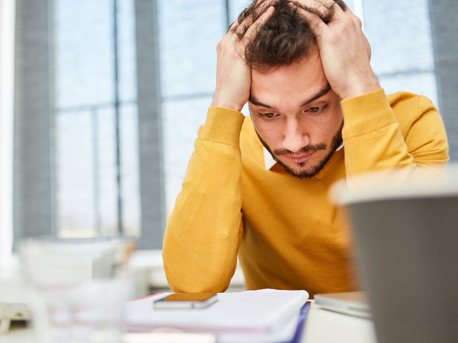 Ein Angestellter mit verzweifeltem Blick starrt auf seinen Schreibtisch. Er plant eine Eigenkündigung wegen Krankheit.
