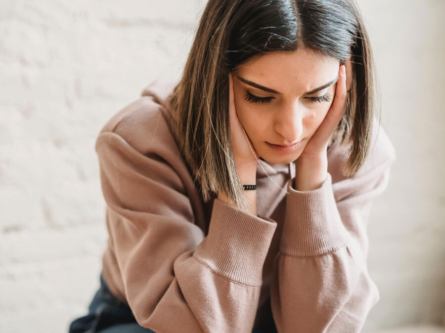 Eine junge Frau schaut bestürzt zum Boden. Sie stützt den Kopf in beide Hände. Sie hat soeben eine Kündigung im Urlaub erhalten.