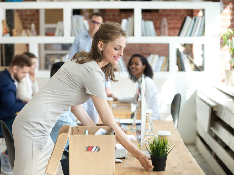 Eine lachende Frau richtet sich im Büro einen Schreibtisch ein.