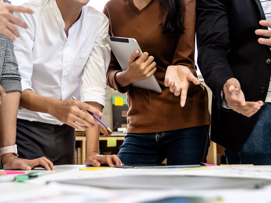 Mitarbeiter stehen um einen Konferenztisch und gestikulieren. Sie führen eine Krisenkommunikation.