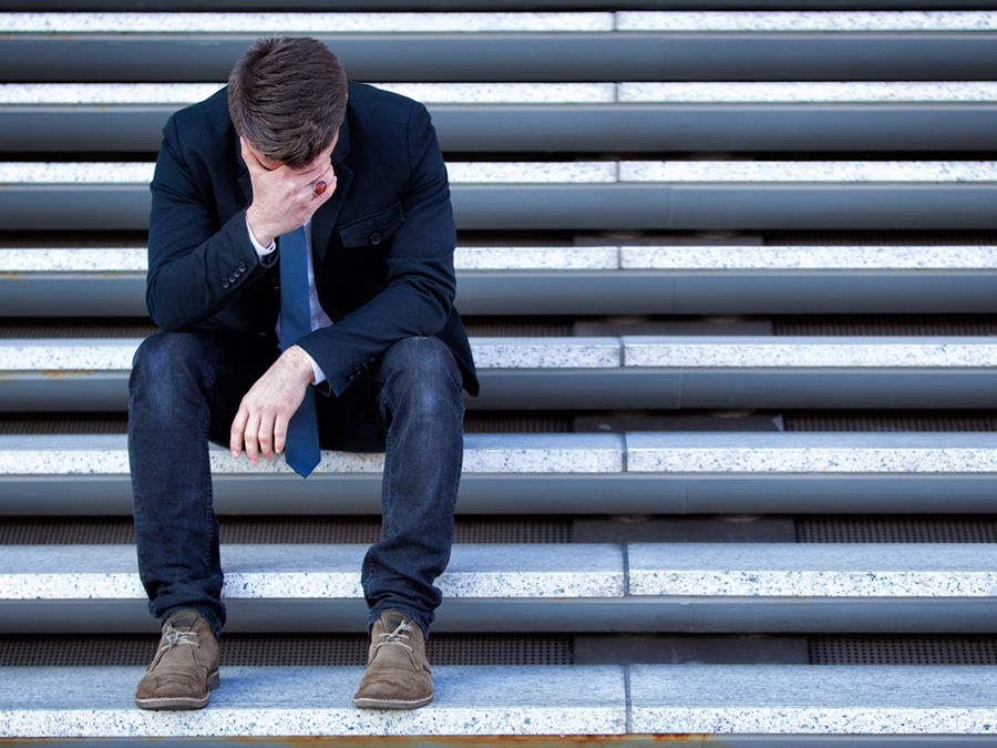 Ein Mann sitzt auf einer Treppe und verbirgt den Kopf in seinen Händen. Er wirkt verzweifelt.