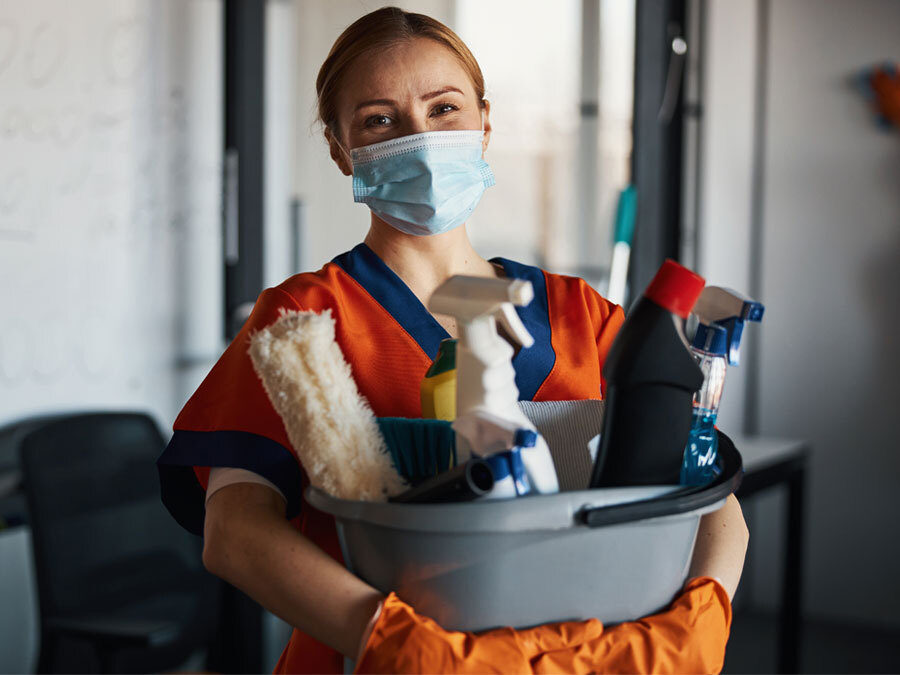 Eine Hausmeisterin hält Putzmaterial in den Händen.