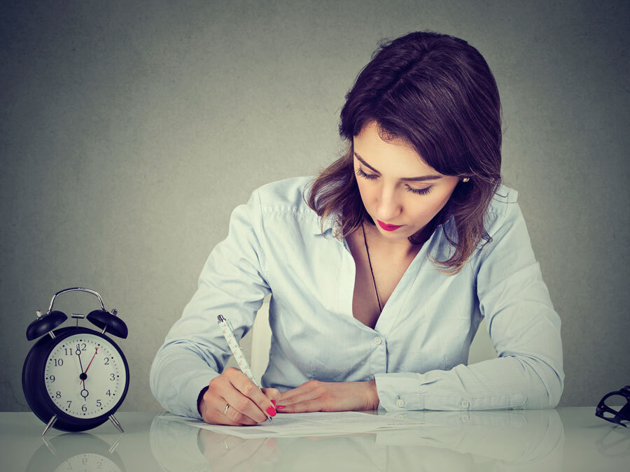 Eine Frau sitzt arbeitend an einem Schreibtisch. Neben ihr tickt ein Wecker und symbolisiert, dass sie sich noch in der Probezeit befindet.