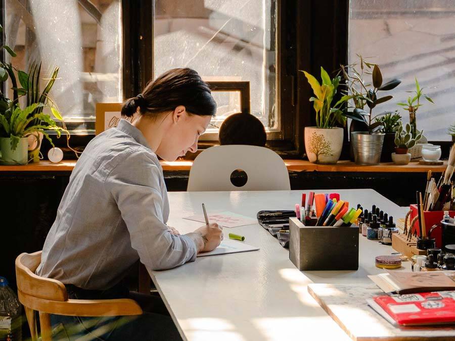 Ein Frau sitzt an einem sonnigen Schreibtisch und schreibt einen Urlaubsantrag.