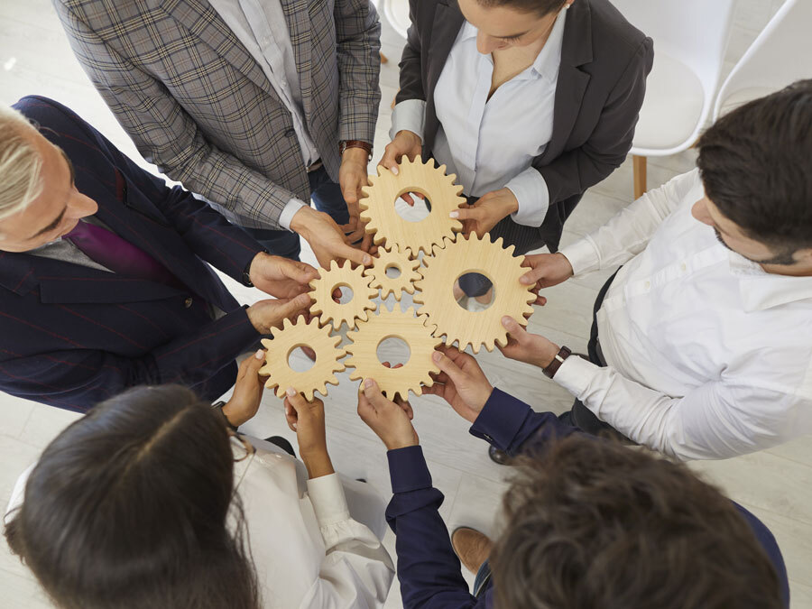 Mehrere Unternehmer halten Zahnräder in den Händen. Sie symbolisieren Managementsysteme.