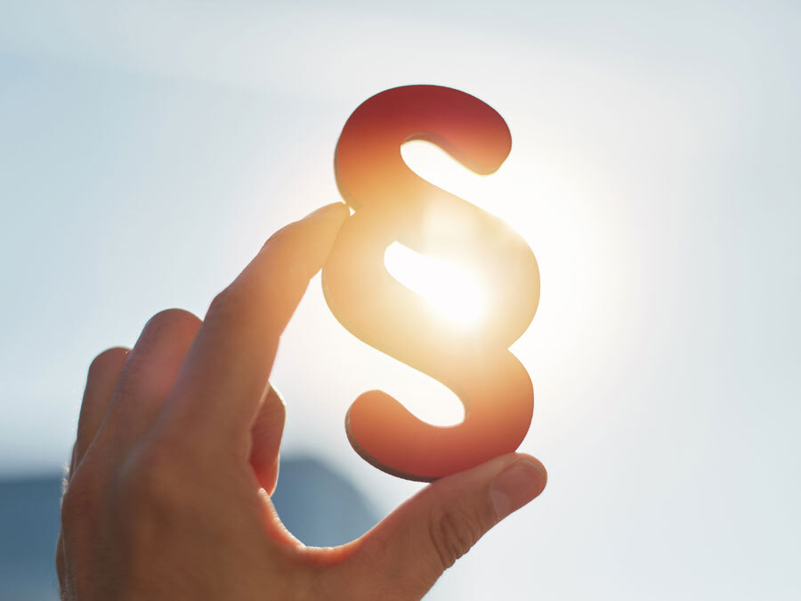 Eine Hand hält ein Paragraphenzeichen in die Sonne.