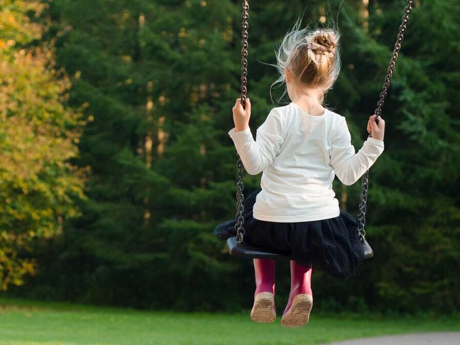 Ein kleine Mädchen sitzt auf einer Schaukel.