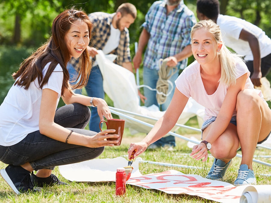 Zwei Frauen malen im Park Plakate für ihre ehrenamtliche Tätigkeit