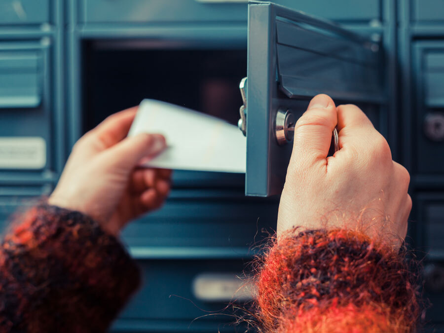 Eine Frau holt einen Brief aus dem Briefkasten.