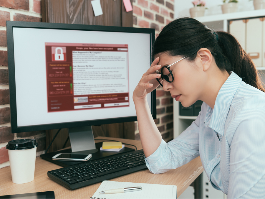 Eine Frau schaut verzweifelt. Sie sitzt vor einem Rechner, der von Computerviren befallen ist.