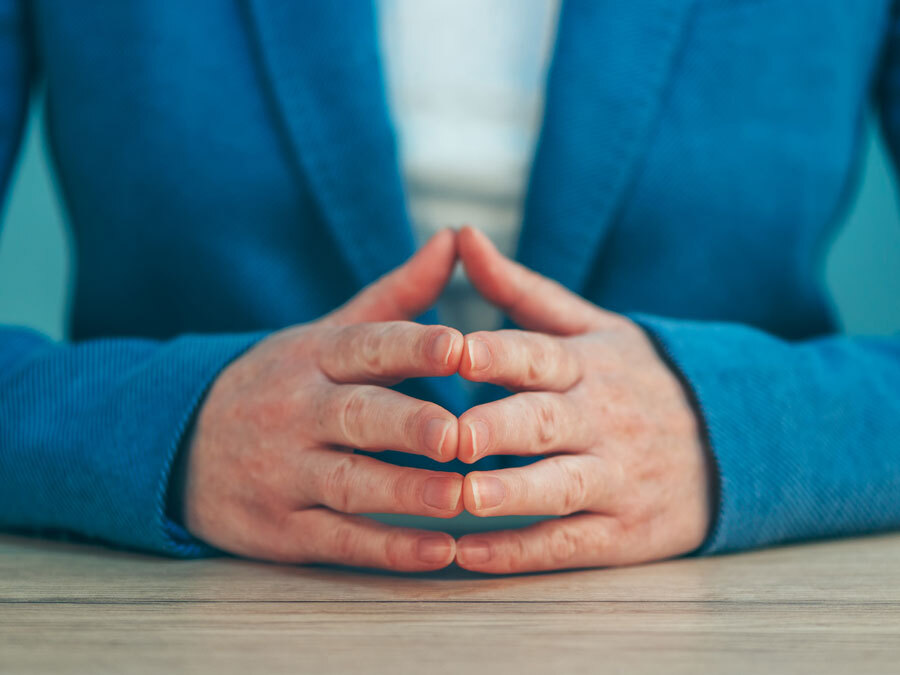 Ein Mann im Anzug sitzt macht eine abwartende Geste.