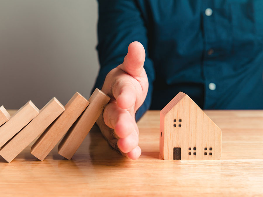 Eine Hand schütz ein kleines Holzspielzeughaus vor dem Umsturz. Es wird das Thema Darlehen sympolisiert.
