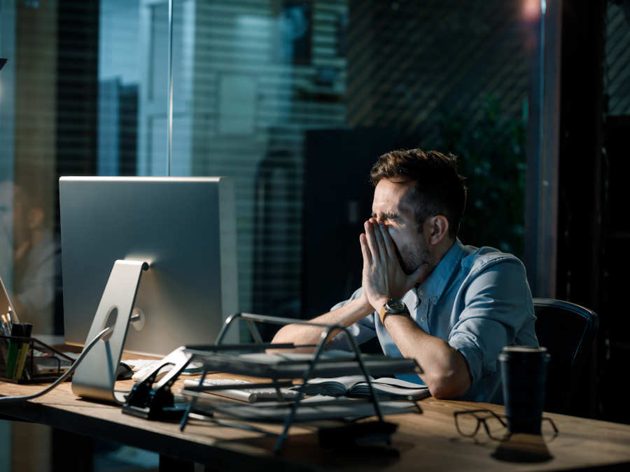 Ein Mann sitzt gähnend im Büro vor einem Bildschirm.