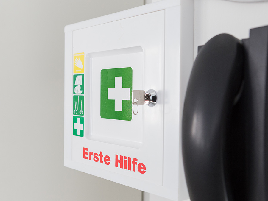 Ein Betriebsverbandkasten hängt an der Wand neben einem Notfalltelefon.