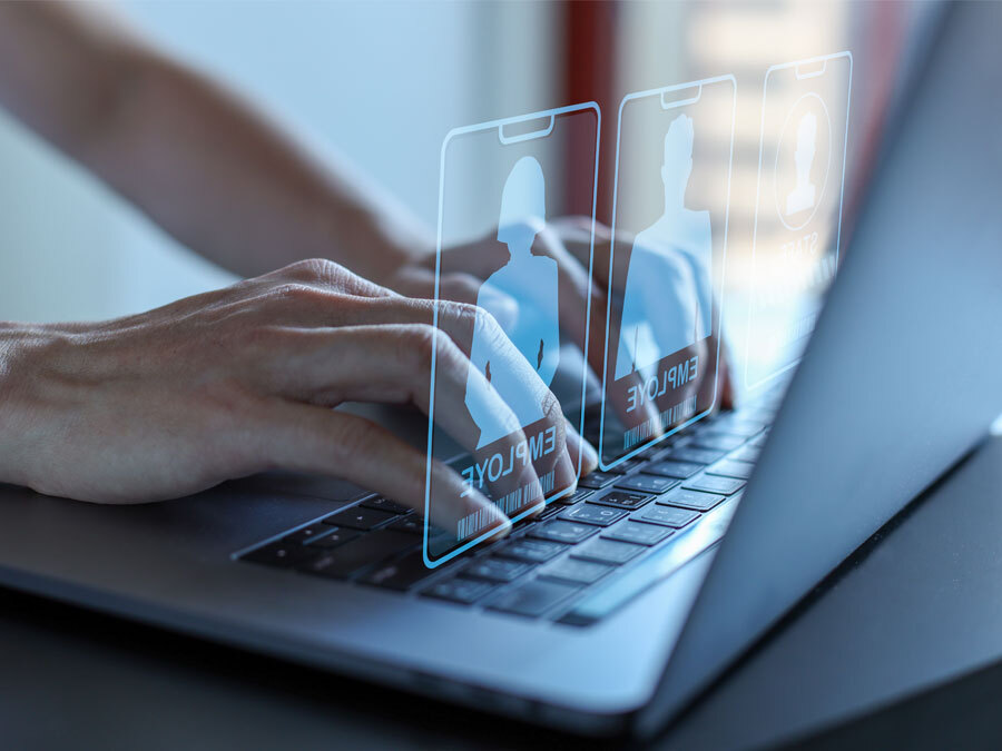 Zwei Hände an einem Laptop tippen Mitarbeiterdaten ein.