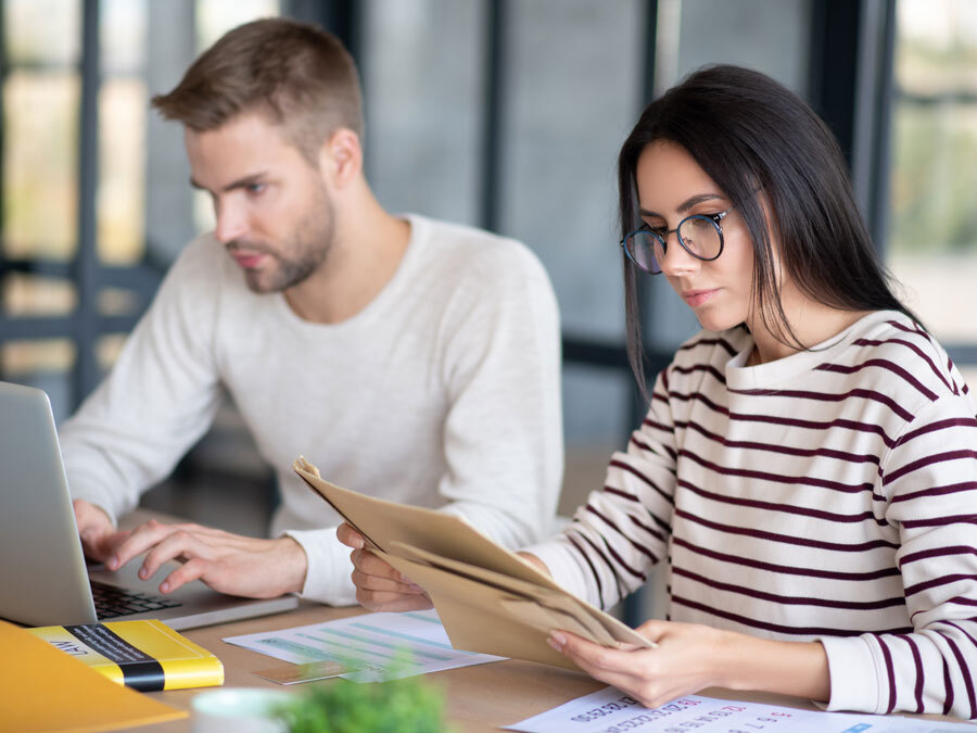 Ein Mann und eine Frau sitzen am Schreibtisch und schauen sich vertrauliche Unterlagen an.